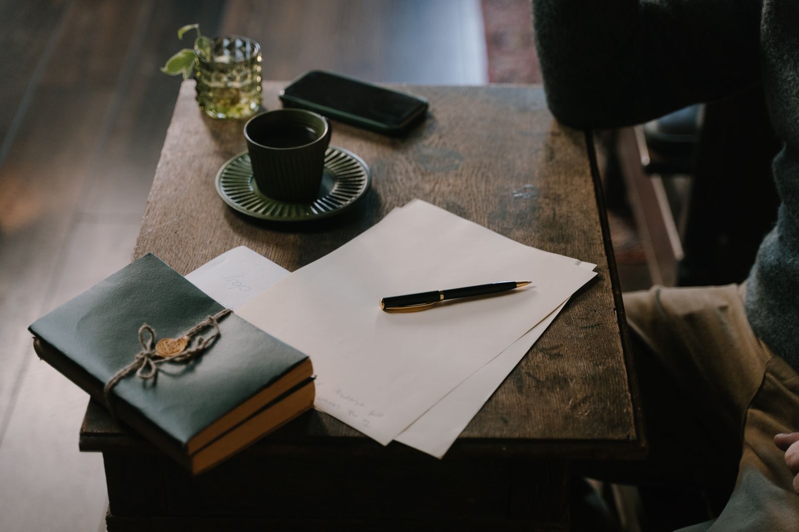 A bound ledger, loose papers and a pen resting on a dark wooden desk.